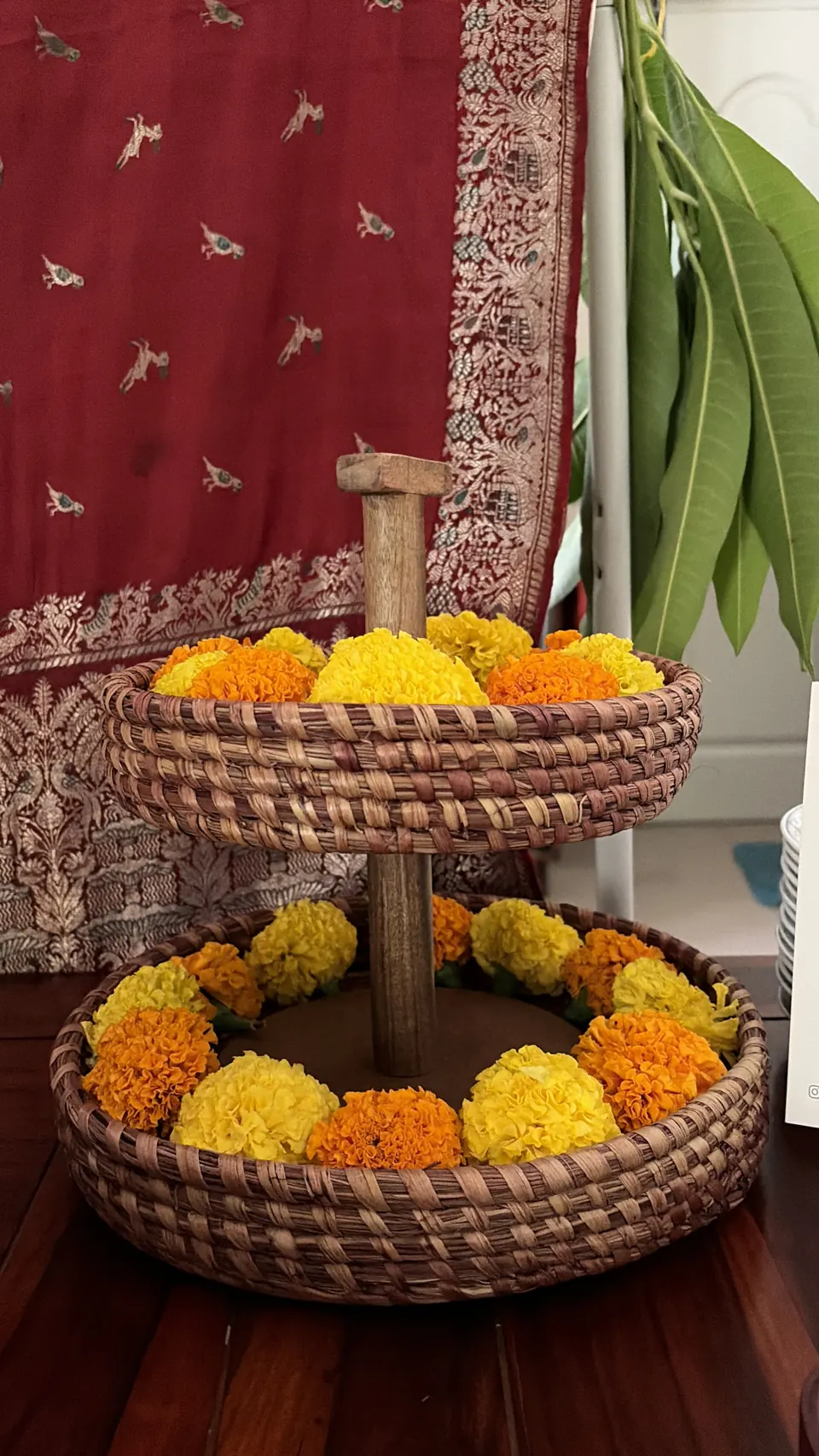 Two-tier woven basket overflowing with orange and yellow marigolds against a red-and-gold brocade sari