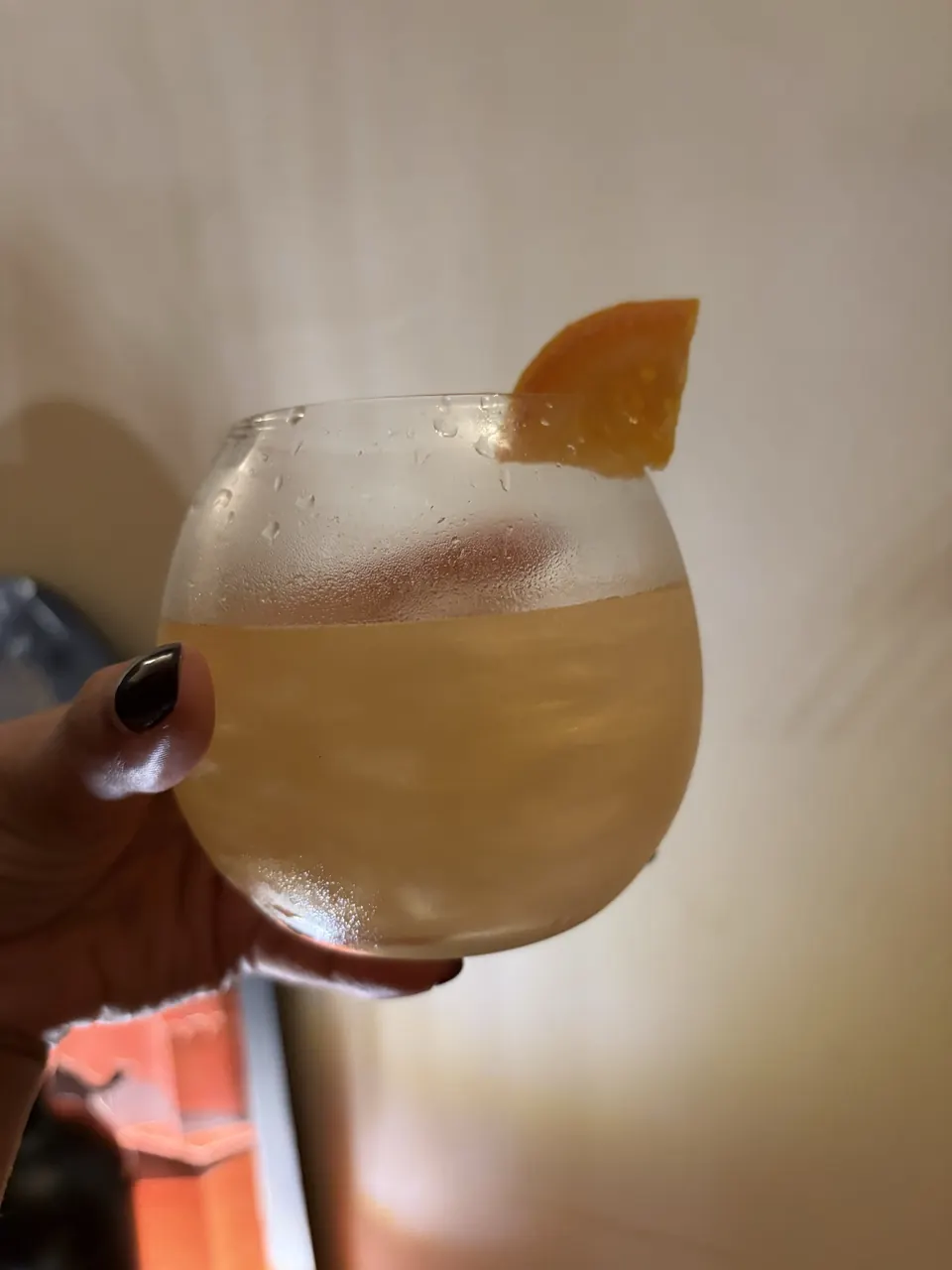 Hand raising a balloon glass of gin and tonic garnished with an orange slice