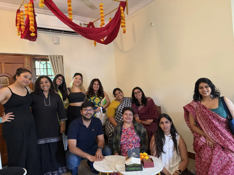 Group of smiling guests in saris and kurtas posing beneath marigold-garlanded maroon drapes