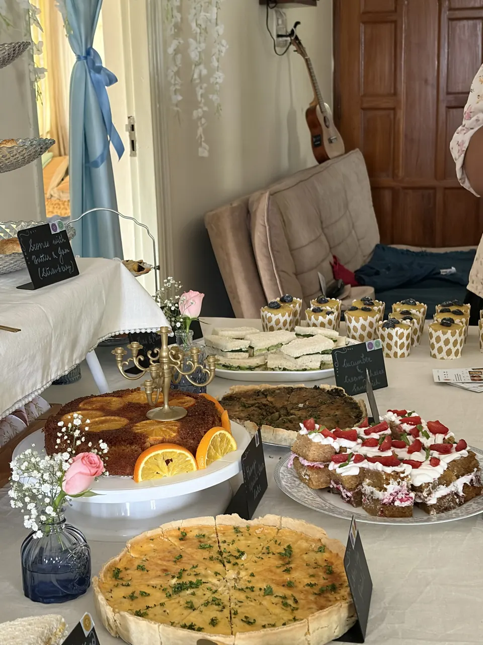 Orange upside-down cake under a gold candelabra beside a herbed quiche and strawberry-topped Victoria sandwich