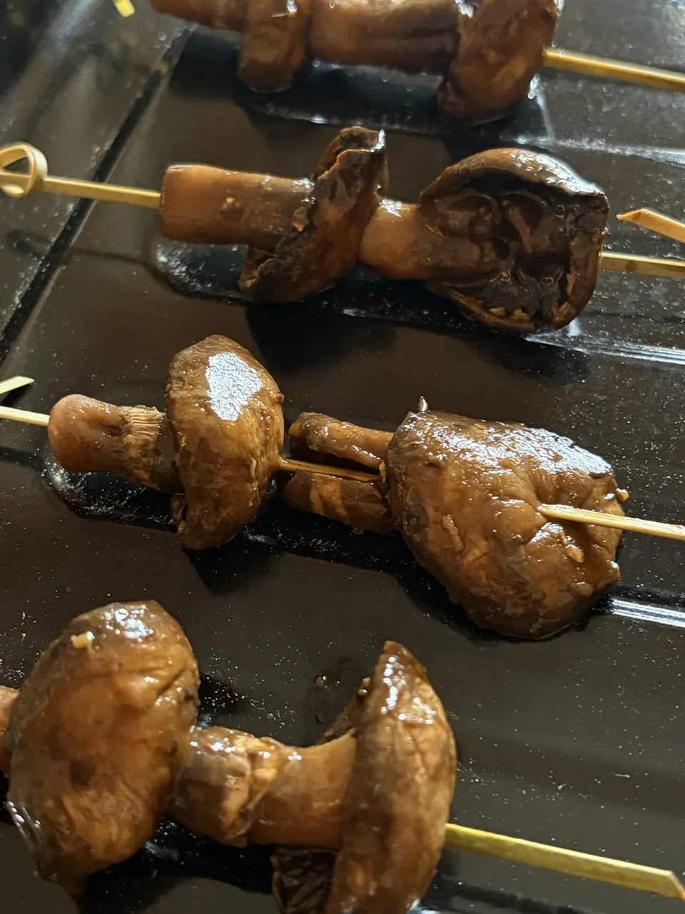 Close-up of glossy teriyaki mushroom skewers on bamboo sticks resting on a dark tray