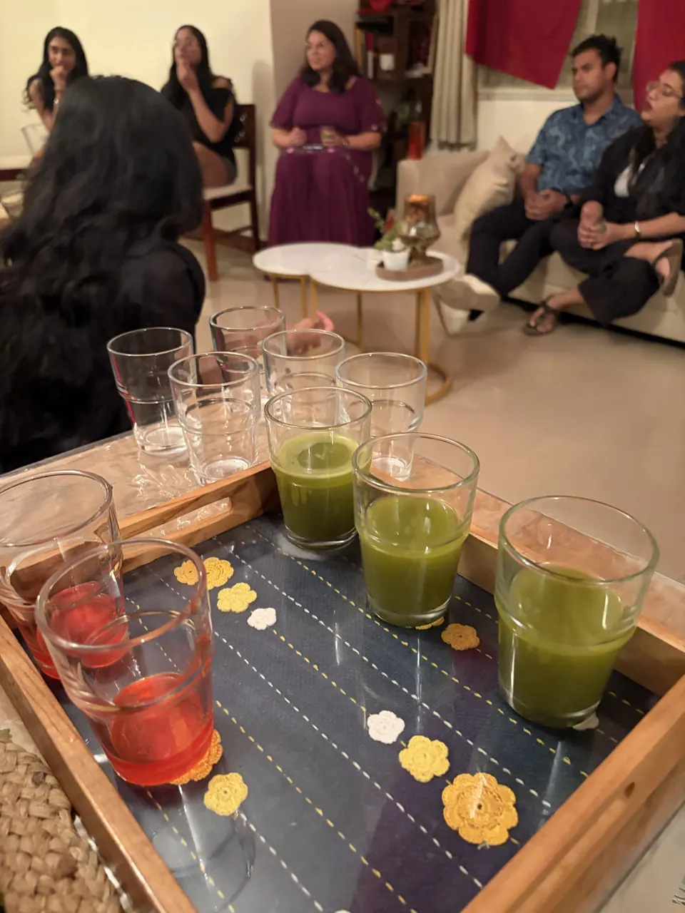 Tray of green and red drinks in glasses on a navy cloth dotted with crocheted yellow flowers