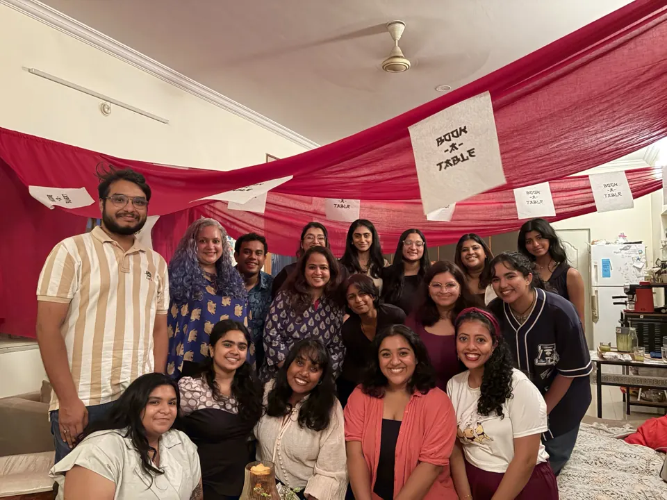 Smiling group of around twenty guests and hosts posing under red drapes and Book-A-Table banners