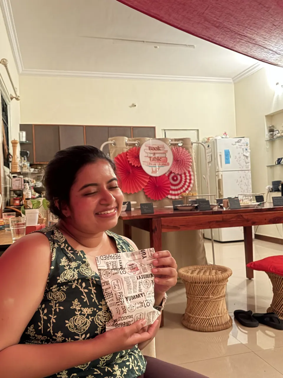 A guest laughs with eyes closed, holding a printed paper food wrap in a decorated living room