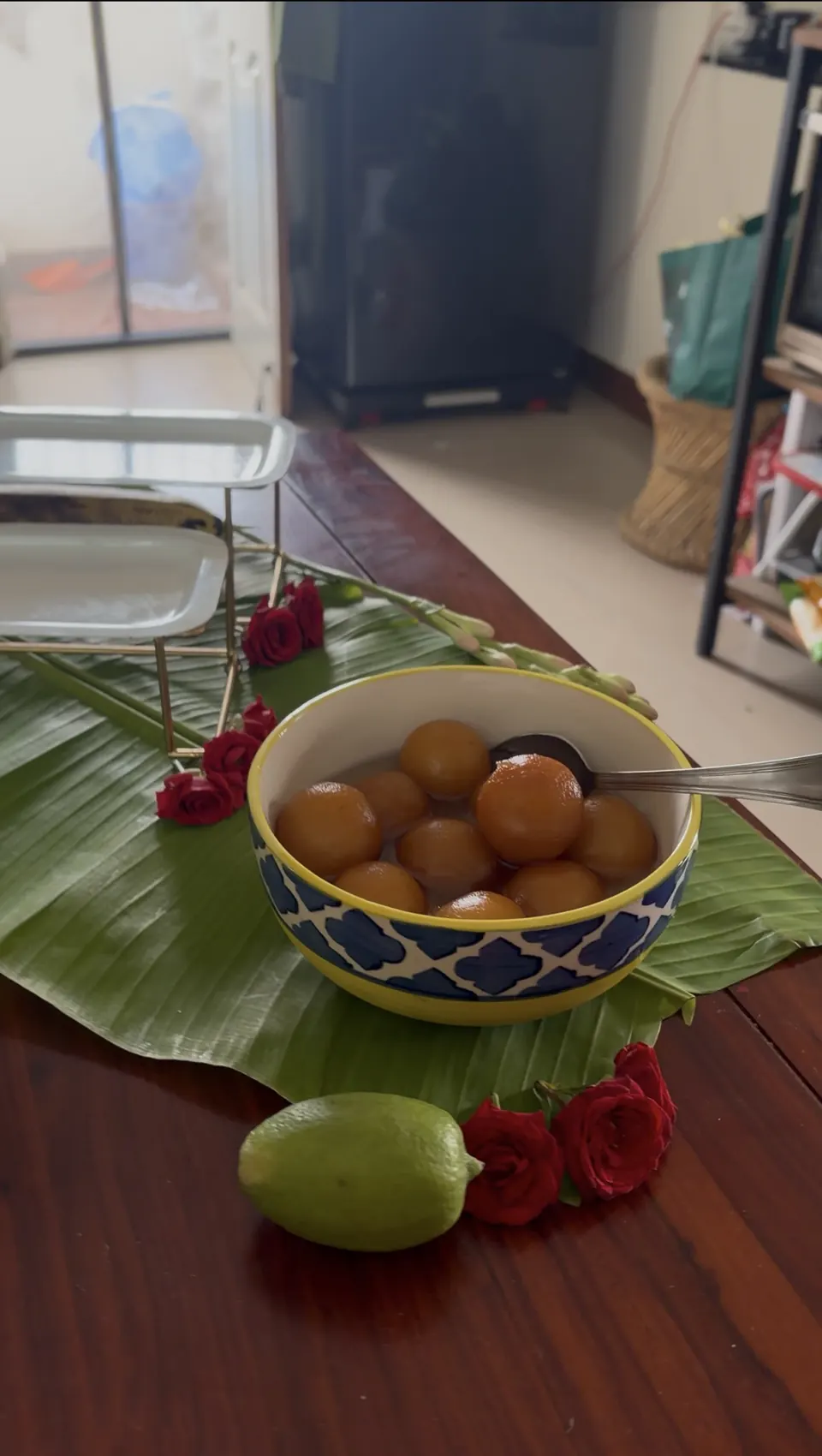 Golden syrup-soaked sweets in blue mosaic bowl on banana leaf with roses and lime