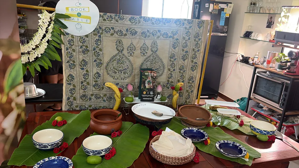 Empty buffet table dressed with banana leaves, clay pots, blue floral bowls, roses and indigo kantha backdrop