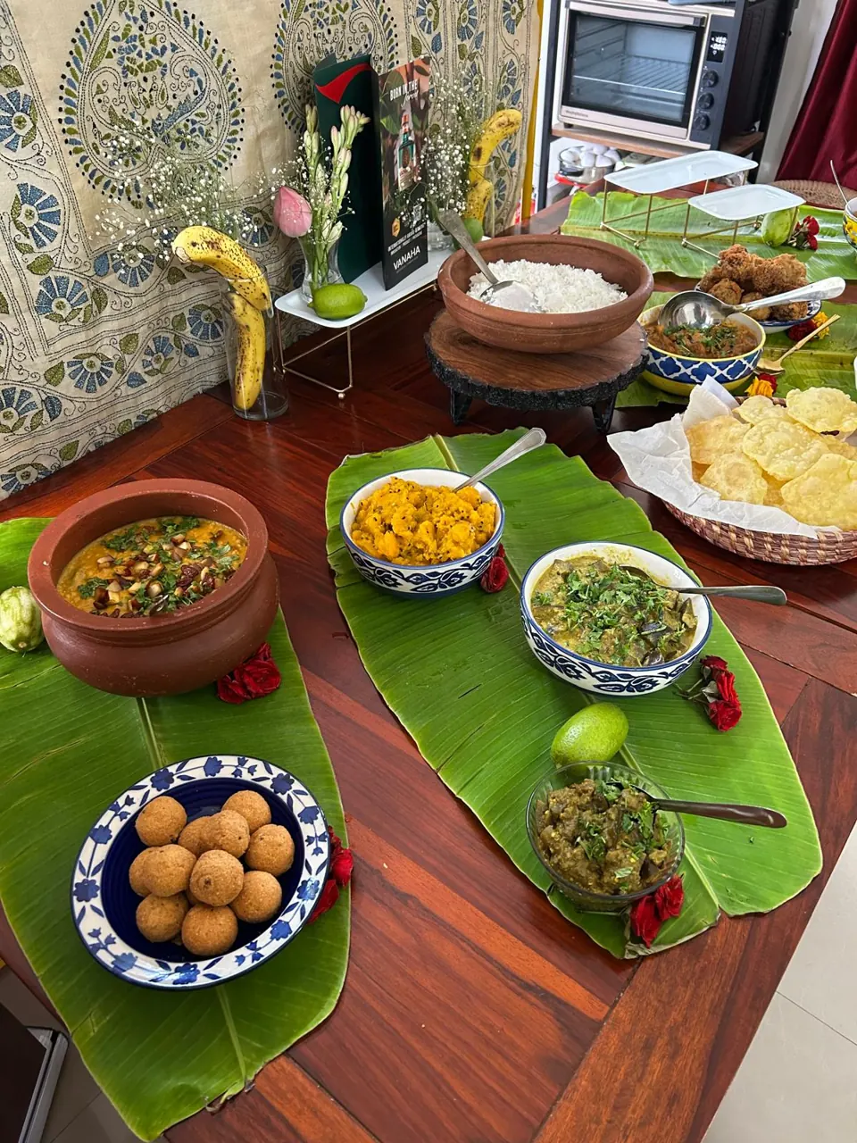Overhead view of Bengali dishes on banana leaves: dal in clay pot, aubergine curry, croquettes, papad