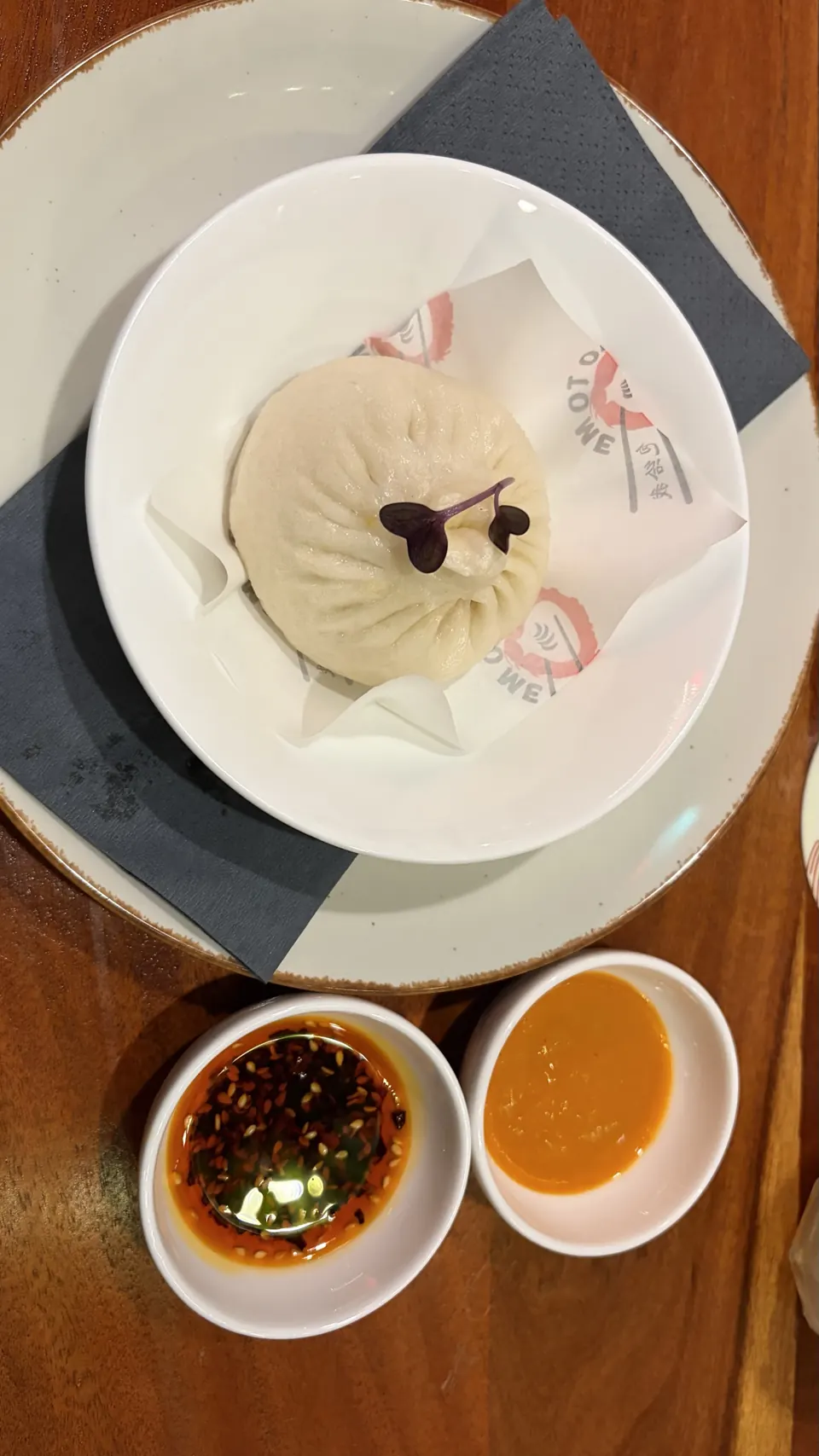 Steamed bao topped with purple microgreens on Bao To Me paper, with chilli oil and orange dipping sauce